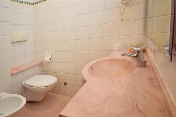 Kúpeľňa s umývadlom, toaletou a bidetom v bledoružovej farbe s bielymi obkladačkami.