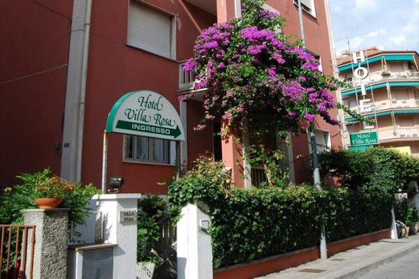 Vchod do hotela Villa Rosa obklopený kvitnúcimi rastlinami.