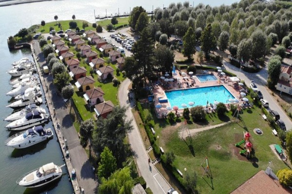 Letecký pohľad na rekreačný areál s bazénom, bungalovmi, loďami a detským ihriskom pri vode.