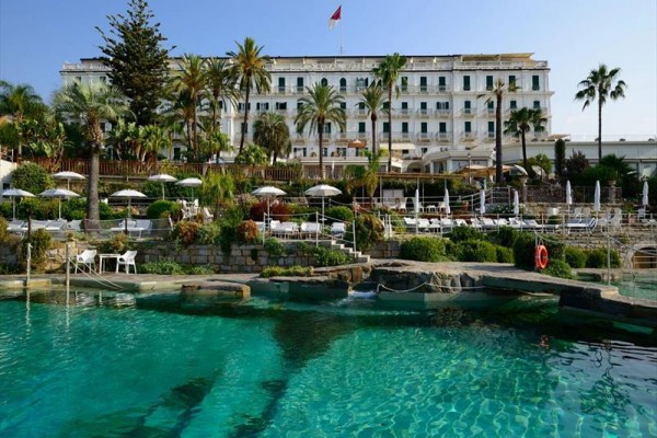 Luxusný hotel s bazénom obklopený palmami a slnečníkmi.