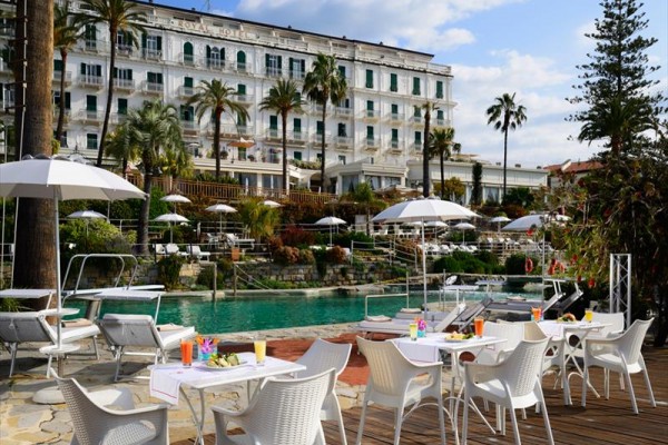 Luxusný hotel s bazénom a vonkajšími stolmi obklopený palmami.