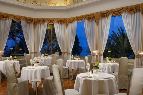 Elegantná reštaurácia s okrúhlymi stolmi a veľkými oknami s výhľadom na vonkajšiu scenériu.
