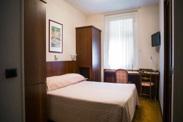 Jednoducho zariadená hotelová izba s posteľou, stolíkom, stoličkou a televízorom na stene.