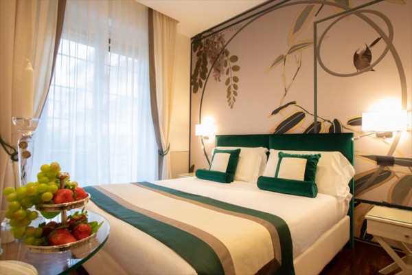 Elegantná hotelová izba s manželskou posteľou, štýlovým nábytkom a ozdobnými vankúšmi.