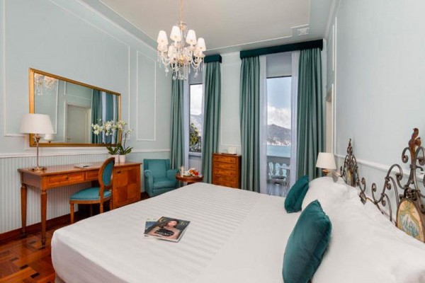 Elegantná hotelová izba s veľkou posteľou, písacím stolom a balkónom s výhľadom na hory.