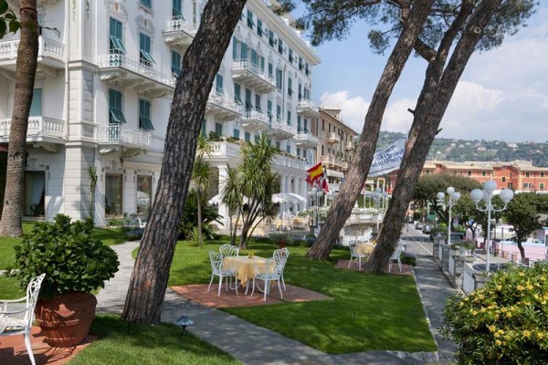 Hotel s bielou fasádou obklopený záhradou s posedením.