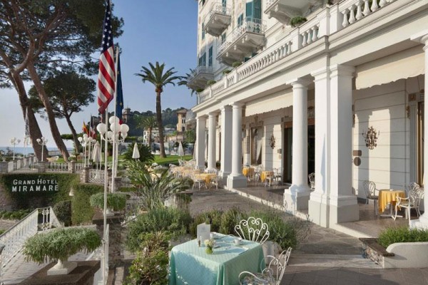 Vonkajšia terasa Grand Hotelu Miramare s výhľadom na more, ozdobená zeleňou a americkou vlajkou.