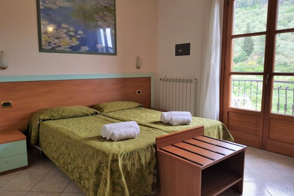 Izba s dvomi posteľami s dekami, drevený nábytok a balkón s výhľadom na zeleň.  