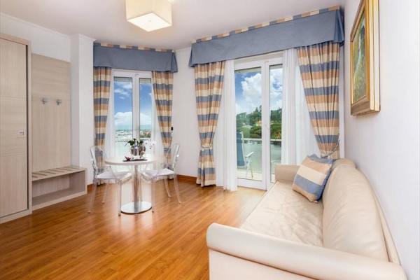 Svetlá obývacia izba s pohovkou, okrúhlym stolom, stoličkami a výhľadom na mesto z balkóna.