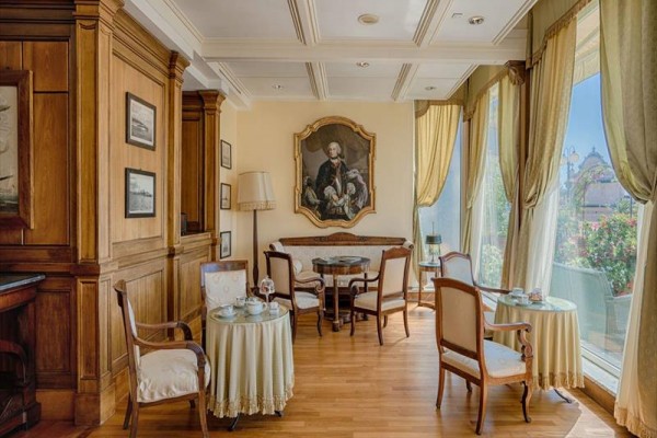 Elegantná kaviareň s dreveným obložením, starožitným nábytkom a obrazom muža na stene.