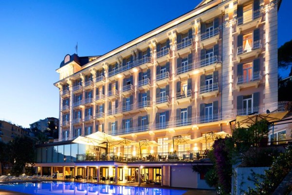 Luxusný hotel s osvetlenou fasádou a vonkajším bazénom za súmraku.