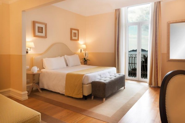 Elegantná hotelová izba s veľkou posteľou a výhľadom na more z balkóna.