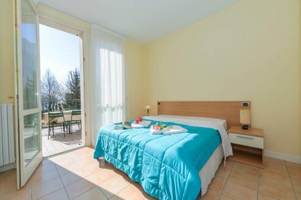 Svetlá spálňa s posteľou s modrou prikrývkou a otvorenými dverami na balkón.