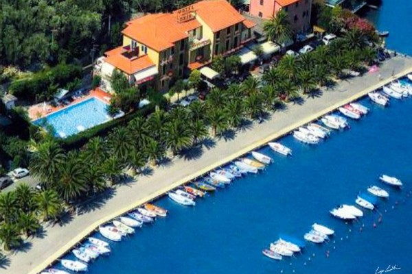 Hotel s bazénom pri pobrežnej promenáde lemovanej palmami a člnmi.