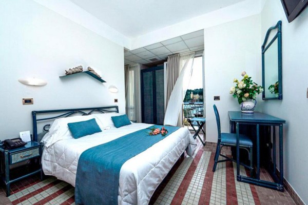 Elegantná spálňa s veľkou posteľou, modrými doplnkami a balkónom s výhľadom von.