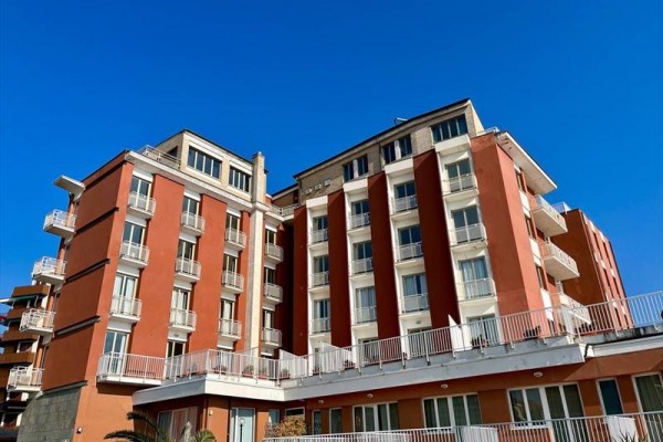Červená budova s viacerými balkónmi pod modrou oblohou.  