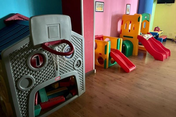 Detský kútik s farebnými plastovými šmykľavkami a preliezkami na drevenej podlahe.