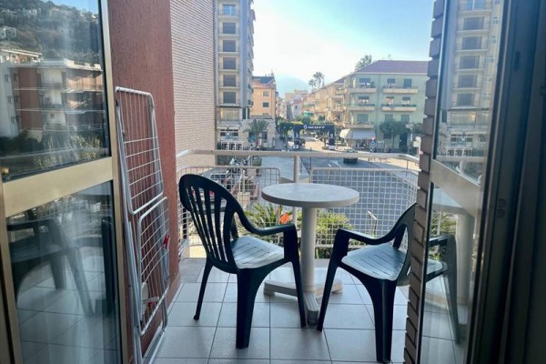 Malý balkón s plastovým stolíkom a dvoma stoličkami, s výhľadom na mestskú ulicu.