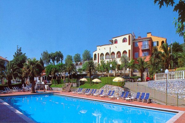 Bazén s ležadlami a žltými slnečníkmi pred farebným hotelom obklopeným palmami.