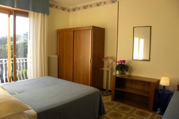 Hotelová izba s manželskou posteľou, skriňou a balkónom.