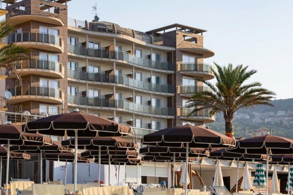 Moderný hotel s balkónmi a palmy pred ním.  