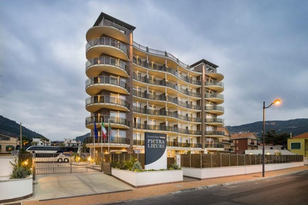 Moderný viacposchodový hotel s balkónmi a sklenými zábradliami za súmraku.