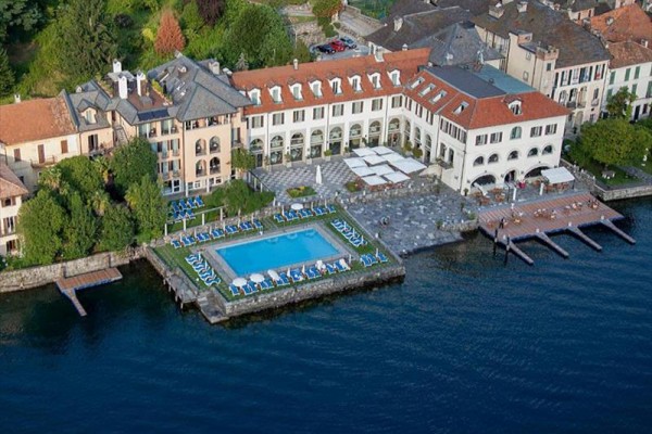 Hotel s bazénom pri jazere obklopený zeleňou.