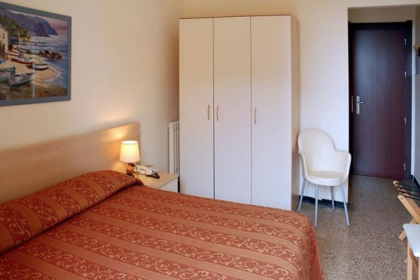 Útulná spálňa s dvojlôžkom, skriňou a nástenným obrazom prímorskej scenérie.  