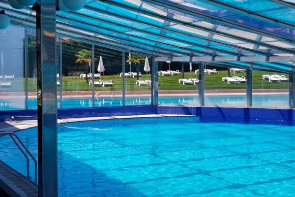 Krytý bazén s priehľadnou strechou a vonkajším výhľadom na lehátka a slnečníky.