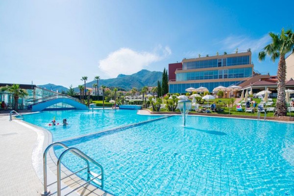 Veľký vonkajší bazén s viacposchodovým hotelom v pozadí a horami na horizonte.