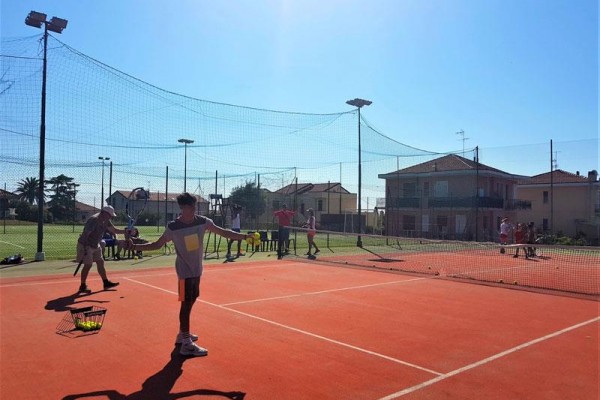 Ľudia hrajú tenis na vonkajšom kurte za slnečného dňa.
