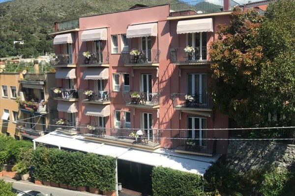 Ružová budova so štyrmi podlažiami a balkónmi s kvetinami.