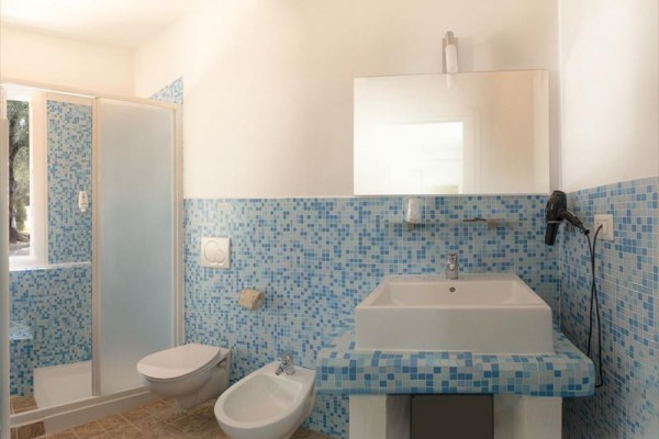 Kúpeľňa s modrou mozaikou obsahujúca sprchovací kút, toaletu, bidet a umývadlo s veľkým zrkadlom.