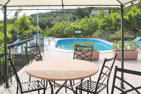 Pergola s okrúhlym stolom a stoličkami pri vonkajšom bazéne na terase.