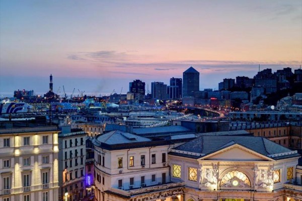 Pohľad na večerné mesto s osvetlenými budovami a prístavom na horizonte.