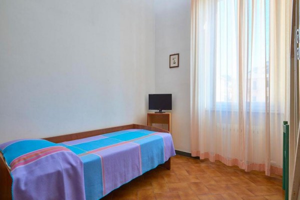 Jednolôžková izba s modro-ružovým prehozom a malou televíziou pri okne s priesvitnými záclonami.