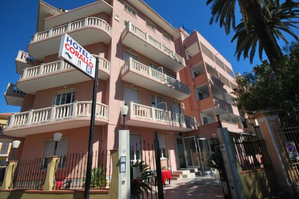 Ružový hotel s viacerými balkónmi a palmou pri vchode.