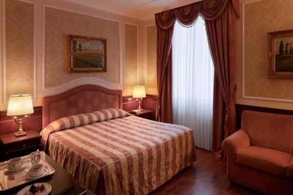 Elegantná hotelová izba s veľkou posteľou a hnedými závesmi.