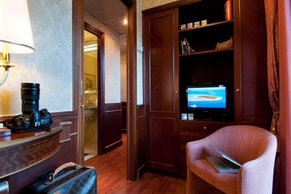 Luxurious hotelová izba s televízorom, fotoaparátom na stole a otvoreným kufrom na zemi.