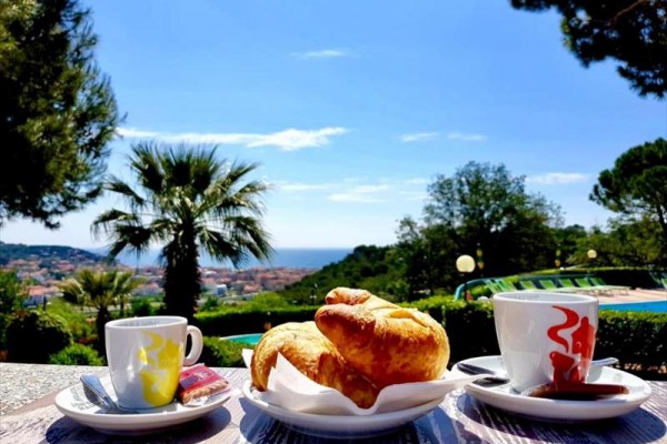 Šálky kávy a croissanty na stole s výhľadom na krajinu pri mori.