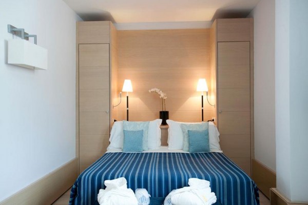 Elegantná spálňa s manželskou posteľou a modrým prehozom pod dvoma lampami.