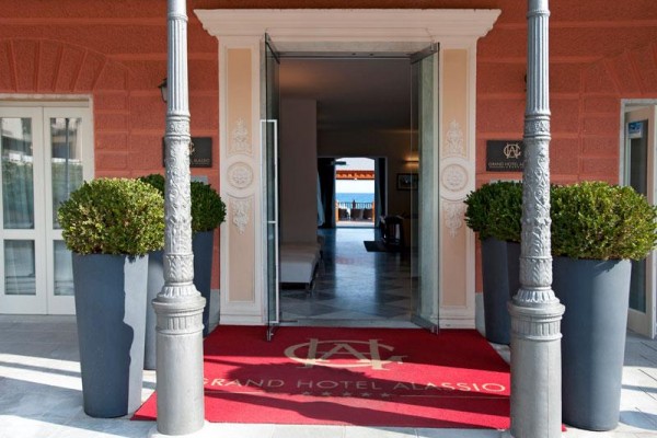 Vchod do Grand Hotelu Alassio s otvorenými dverami a červeným kobercom.