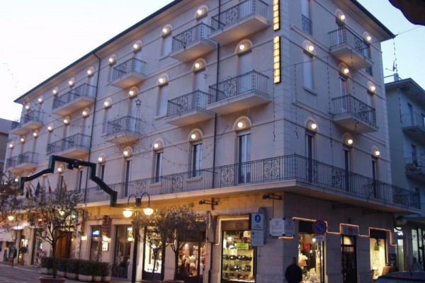 Osvetlená budova s balkónmi na rohu ulice večer.