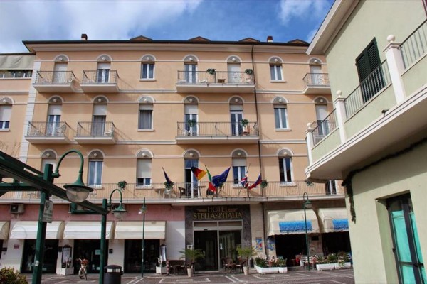 Budova hotela s balkónmi a vlajkami pri vchode.
