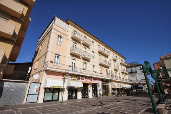 Budova s obchodmi na prízemí a balkónmi nad nimi na pozadí modrej oblohy.