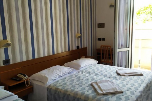 Izba s dvoma posteľami, pruhovanými tapetami a otvorenými dverami na balkón.