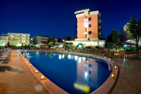 Nočný pohľad na vonkajší bazén pred osvetleným hotelom Apollo.