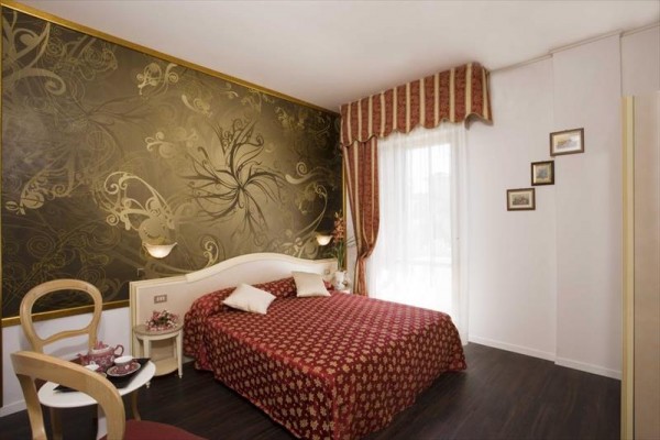 Elegantná hotelová izba s dvojlôžkom a výraznou zlatou tapetou.