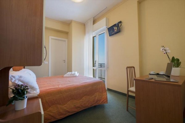 Svetlá izba s posteľou, písacím stolom, televízorom a balkónom s výhľadom.