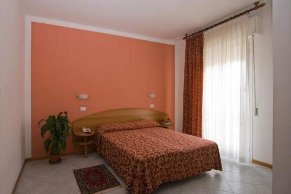 Spálňa s oranžovou stenou, manželskou posteľou, rastlinou a závesom na okne.  